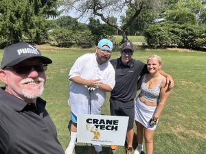 Four golfers pose together on the course next to a Crane Tech sponsorship sign at the McKeesport golf outing.